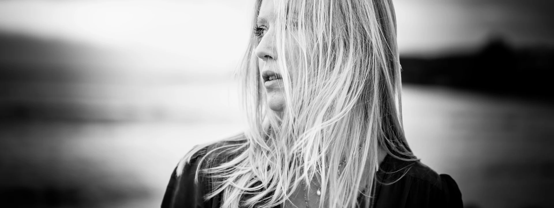 Portrait en noir et blanc d'une femme, cheveux au vent au bord de l'eau