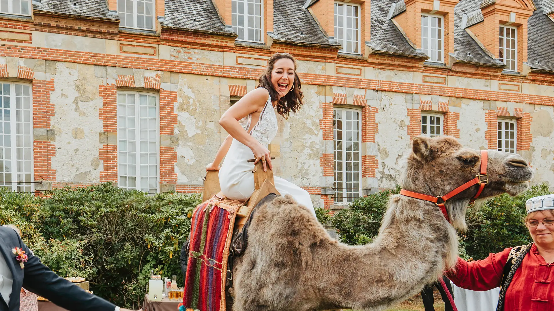 Mariée riant aux éclats, assise sur un chameau devant un château
