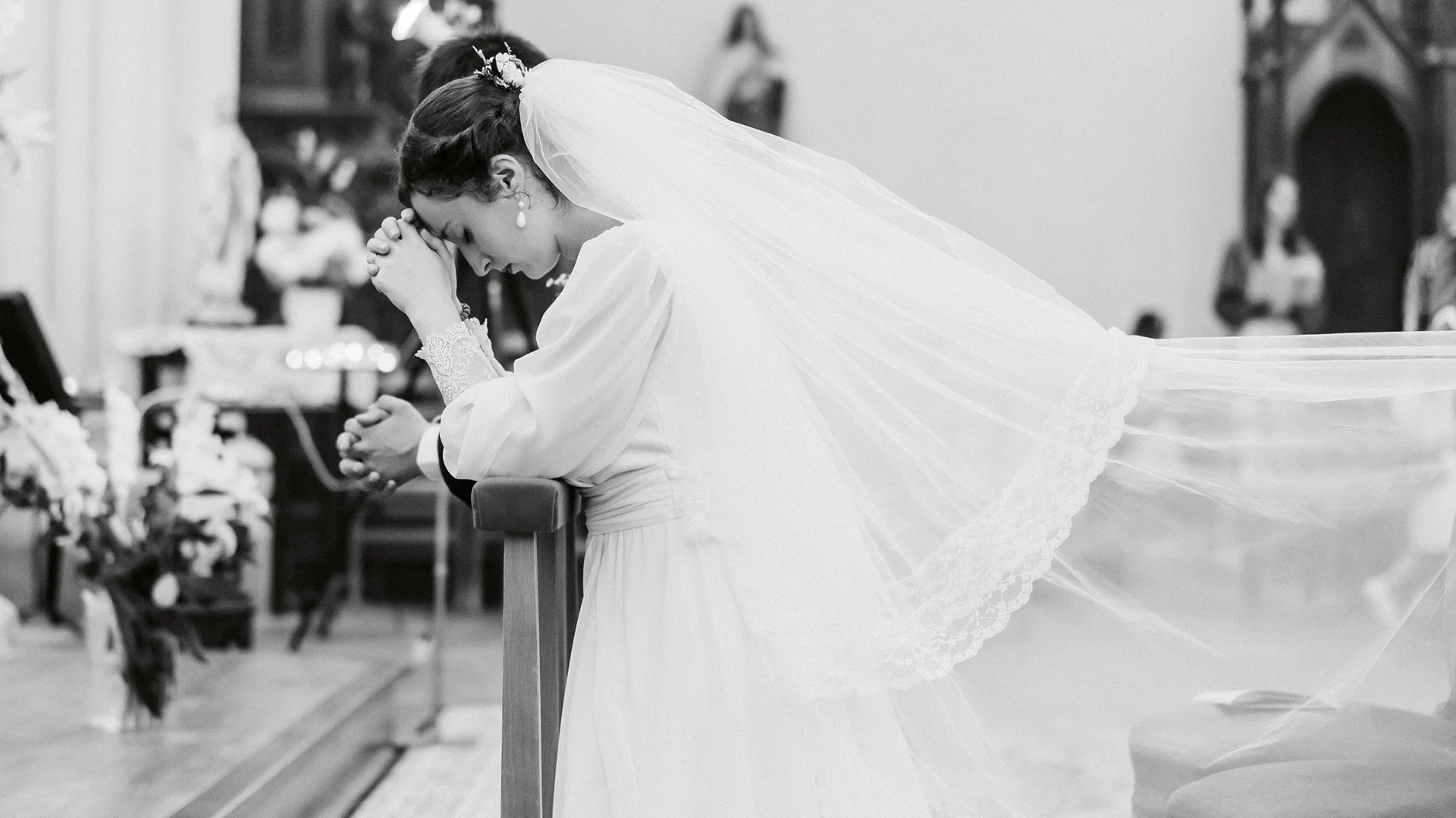 Mariée en noir et blanc, le visage dans les mains, longue traîne de voile dans une église