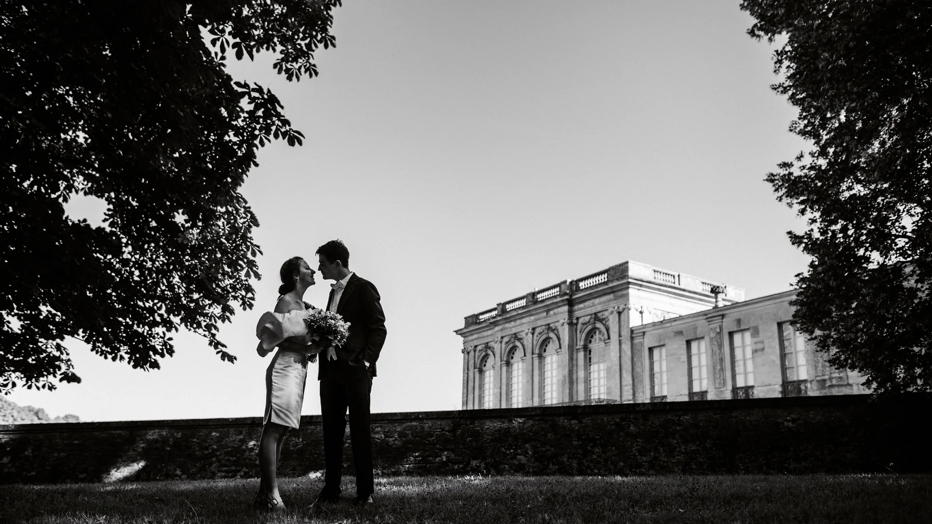 Couple de mariés en noir et blanc devant l'Orangerie, sous les grands arbres