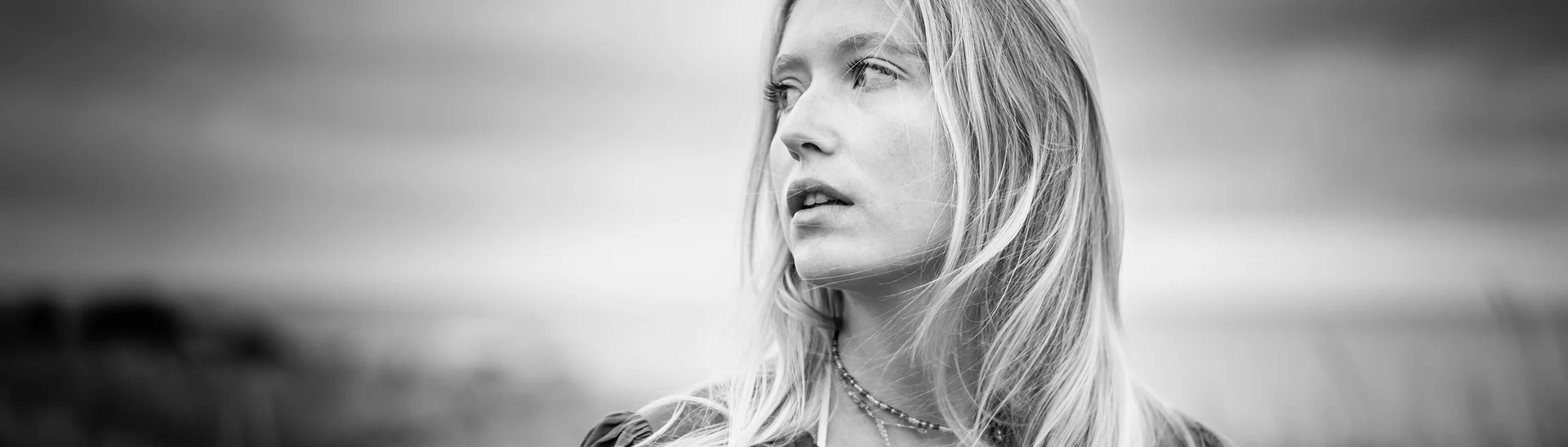 Portrait en noir et blanc d'une femme, cheveux au vent au bord de l'eau
